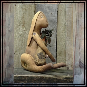 Puede incluir: Un conejo de tela marrón con una nariz de botón y una zanahoria en la mano. El conejo está sentado sobre una superficie de madera.