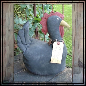 May include: Black fabric chicken with a red comb and a tag that says "Old Hen" hanging from its neck. The chicken is sitting on a wooden surface.