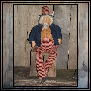 May include: A handmade rag doll dressed in a blue jacket, red and white striped trousers, and a black top hat. The doll is sitting on a wooden crate against a wood panel background.