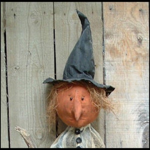 May include: A handmade rag doll witch with a black pointed hat, orange face, and brown hair. The doll is holding a stick broom in its hand.