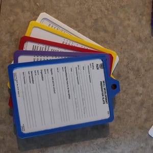 May include: A stack of coloured training slates with white paper inserts. The slates have blue, red, yellow, purple, and white frames. The text "SKILL DEVELOPMENT PREPARATION SLATE" is visible on one slate.