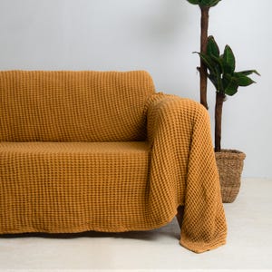 Könnte beinhalten: Eine senfgelbe Waffel-Decke, die über ein Sofa gelegt ist. Die Decke ist weich und strukturiert und wäre perfekt, um jedem Wohnzimmer einen Hauch von Wärme und Stil zu verleihen.