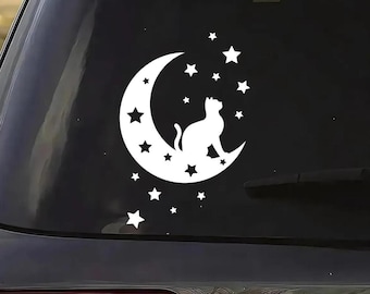 May include: A white vinyl decal applied to a dark car window, featuring a silhouette of a cat sitting on a crescent moon surrounded by various sizes of stars. The design is solid white and creates a high-contrast graphic on the glass surface.