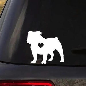 May include: White vinyl decal of a bulldog silhouette with a heart in its chest. The decal is on the back window of a black car.