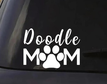 May include: White vinyl decal applied to a car window. The decal reads "Doodle Mom" in a script font, with the word "Mom" incorporating a paw print design. The decal is likely for dog lovers.