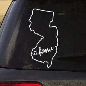 May include: A white vinyl decal of the state of New Jersey with the word "home" written inside the outline of the state. A small heart is in front of the word "home". The decal is on the back window of a black car.
