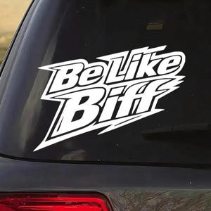 May include: White vinyl sticker with the text "Be Like Biff" in a bold, stylized font, applied to the rear window of a dark-coloured car. The sticker makes a statement.