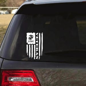 K&ouml;nnte beinhalten: Ein wei&szlig;er Vinyl-Aufkleber mit einer amerikanischen Flagge im Used-Look. Die Flagge tr&auml;gt die Worte "Veteran" vertikal auf der linken Seite und ein USMC-Logo mit den Worten "USMC" darunter auf der rechten Seite.