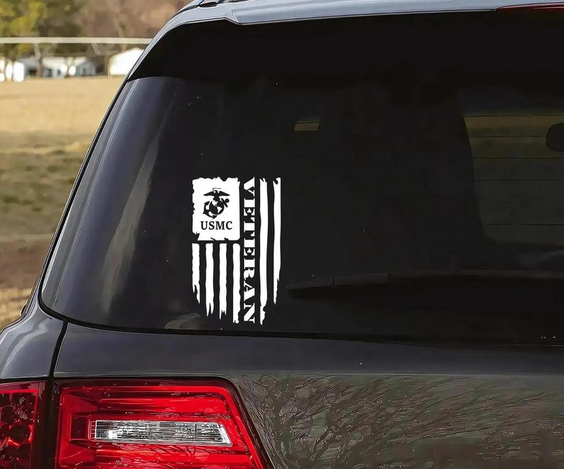 K&ouml;nnte beinhalten: Ein wei&szlig;er Vinyl-Aufkleber mit einer amerikanischen Flagge im Used-Look. Die Flagge tr&auml;gt die Worte "Veteran" vertikal auf der linken Seite und ein USMC-Logo mit den Worten "USMC" darunter auf der rechten Seite.