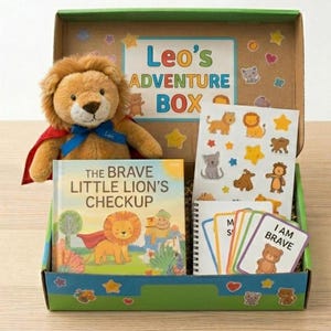 May include: A cardboard gift box labeled Leo's Adventure Box containing a plush lion with a red cape and blue ribbon, a book titled The Brave Little Lion's Checkup, a sheet of animal stickers, and a set of small cards with the text I Am Brave.
