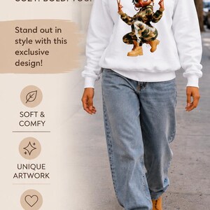 May include: A white long-sleeve sweatshirt featuring a graphic of a cartoon character wearing a camouflage hoodie, camouflage pants, and tan boots, making a peace sign with both hands. The text reads CUTE VIBES ONLY, COZY. BOLD. YOU.