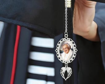 May include: Silver graduation cap charm with a photo frame and angel wings. The photo frame has a picture of an older woman with a smile.