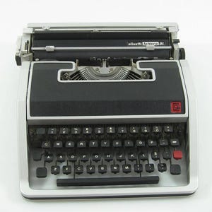 May include: A vintage Olivetti Lettera DL typewriter. The typewriter is black and silver, featuring a full QWERTY keyboard with black keys and white lettering. The model name is displayed on top. A red button is on the right side.