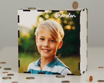 Könnte beinhalten: Ein weißes Sparschwein aus Holz mit einem Foto eines jungen Jungen auf der Vorderseite. Das Foto zeigt den Jungen lächelnd und ein gestreiftes Hemd tragend. Der Name "Brandon" ist in weißen Buchstaben auf der Oberseite des Sparschweins geschrieben.