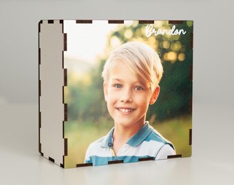 Könnte beinhalten: Holz-Fotobox mit einem Foto eines lächelnden Jungen mit blonden Haaren. Auf der Box steht der Name "Brandon" in Schreibschrift. Die Box besteht aus hellem Holz mit dunklem braunen Rand und einem geschlitzten Design.