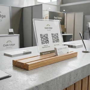 May include: A light-colored wooden display stand holding a clear acrylic sign with the Oakridge Realty logo, two QR codes, and the text Scan for Digital Brochure and Sign-In Here, alongside a stack of business cards for Sarah Johnson, Lead Agent.