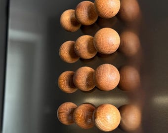 May include: Wooden sphere magnets in a warm brown hue are arranged in rows on a dark gray refrigerator. The magnets have a natural wood grain and a rounded shape, creating a simple, yet elegant design.