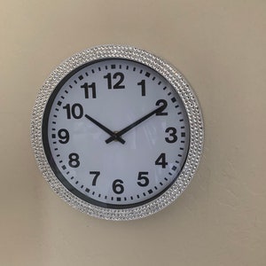 May include: A silver round clock with a white face and black numbers. The clock has a diamond-like design around the edge.