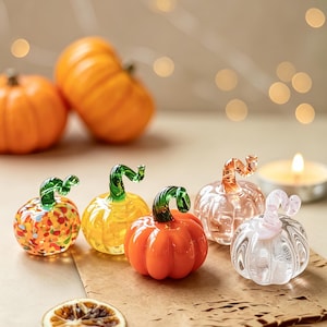 Op de afbeelding: Een collectie van vijf kleine glazen pompoenen met gebogen stelen. De pompoenen hebben verschillende afwerkingen, waaronder transparant, effen oranje, geel en veelkleurige gespikkelde patronen. Elk stuk is voorzien van duidelijke geribbelde texturen.