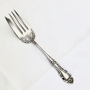 May include: A silver fork with an ornate, detailed handle. The fork has four tines and a pointed tip.