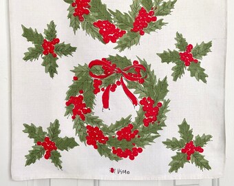 Paño de cocina o camino de mesa navideño de Vera Neumann, guirnaldas de acebo con lazos rojos sobre lino color crema, diseño bidireccional, firmado Vera en ambos extremos.