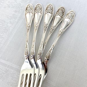 May include: Five silver forks with ornate grape and vine designs on the handles.
