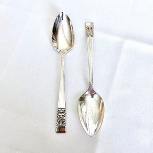 May include: Two silver spoons with ornate handles. The spoons are on a white background.