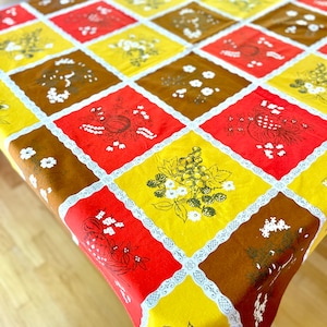 May include: A vintage tablecloth with a repeating pattern of squares in red, yellow, and brown. Each square features a different floral or fruit design in white. The squares are separated by white lace trim, creating a charming, retro aesthetic.