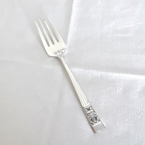 May include: A silver fork with an ornate handle. The handle has a floral design.
