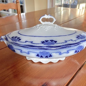May include: A white and blue porcelain serving dish with a lid. The dish has a scalloped edge and a floral design. The lid has a knob on top.