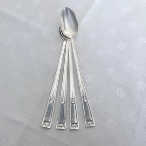 May include: A set of four silver spoons with a classic design. The spoons have long, slender handles with a decorative pattern at the base. The spoon bowls are oval-shaped and polished to a shine. The spoons are arranged on a white surface.