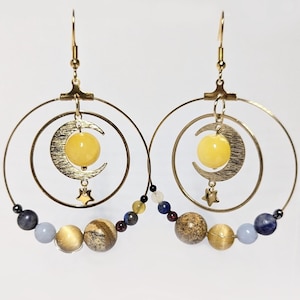 Peut inclure: Boucles d'oreilles créoles dorées avec un pendentif en forme de croissant de lune et une pierre précieuse jaune. Les boucles d'oreilles sont ornées de perles de différentes couleurs, notamment bleu, marron et or.