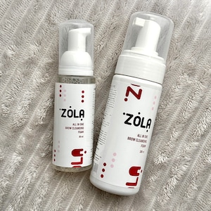 May include: Two white bottles of ZOLA All In One Brow Cleansing Foam. The bottles have a pump dispenser and a clear cap. The labels feature the brand name in a stylized font, along with the product name and volume.