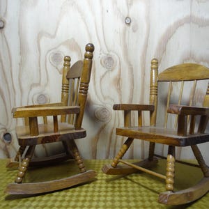以下が含まれることがあります： 明るい茶色の仕上げが施された、2つの小さな木製ロッキングチェア。 椅子は、湾曲したロッキング、アームレスト、スラットバックを備えたクラシックなデザインです。 黄色と緑のチェック柄の表面に、明るい木材の背景に対して表示されています。