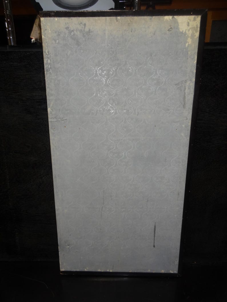 May include: A rectangular, light gray panel with a repeating, swirling pattern. The panel has a black border and appears to be part of a larger structure. The surface shows signs of wear and tear, with some discoloration and scratches.