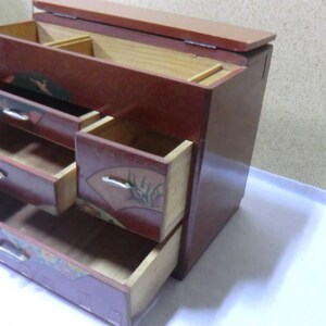 May include: A wooden jewelry box with a red finish and intricate floral designs. The box has four drawers and a hinged lid.