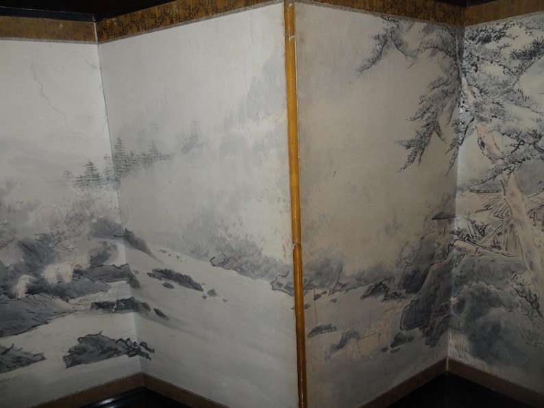 May include: Corner of a room with painted walls depicting a landscape scene in shades of gray and black. The artwork features mountains, trees, and a small building, creating a serene, artistic ambiance. The walls are bordered with a gold trim.