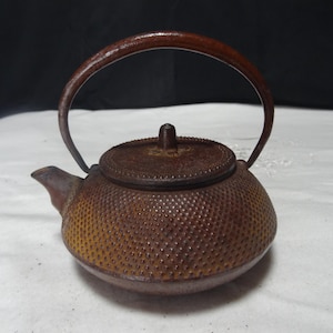 Peut inclure: Une théière en fonte marron avec un corps arrondi et une anse incurvée. La théière a une surface texturée avec de petites bosses et un couvercle avec un petit bouton. Le bec est petit et incliné. La théière est conçue pour infuser du thé.