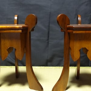 May include: A pair of matching wooden stands, each featuring a flat square top surface supported by four curved legs that extend upward above the platform. The stands are constructed from a medium-brown wood with a smooth, polished finish.