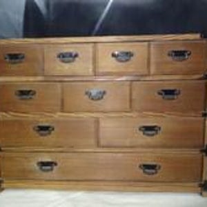 May include: A wooden chest of drawers featuring a light brown finish and dark metal hardware. The unit includes four small top drawers, two medium drawers in the middle, and three large drawers at the bottom, all with rectangular metal pulls.