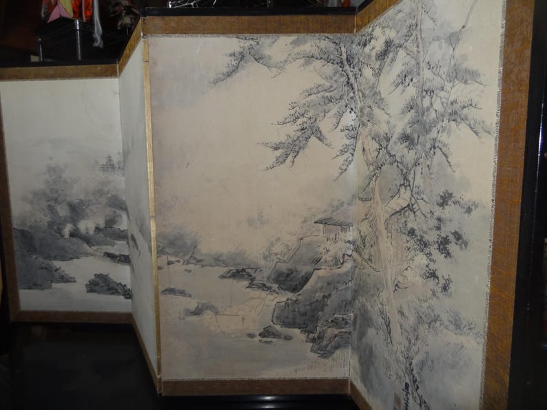 May include: A multi-panel screen featuring a traditional Asian landscape painting. The artwork depicts mountains, water, and trees in shades of gray and white, with a hint of gold trim on the wooden frame.