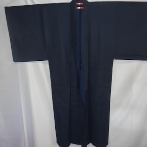 May include: A dark navy blue kimono with wide sleeves, hanging open to reveal a contrasting blue interior. The traditional Japanese garment is displayed against a white backdrop, showcasing its simple, elegant design.