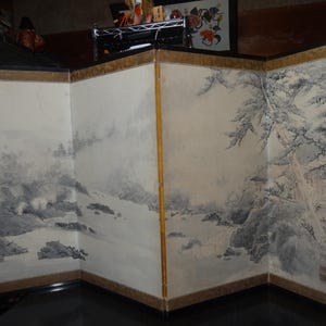 May include: A multi-panel folding screen featuring a landscape painting in shades of gray and white. The artwork depicts mountains, water, and trees, with a gold border. The screen is a decorative piece.
