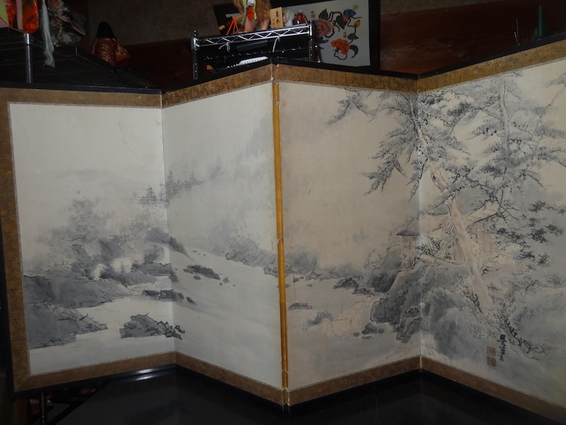 May include: A multi-panel folding screen featuring a landscape painting in shades of gray and white. The artwork depicts mountains, water, and trees, with a gold border. The screen is a decorative piece.