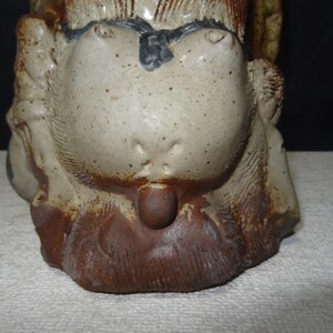 May include: A ceramic sculpture of a stylized animal head, featuring a light beige face with dark brown spots and a dark brown lower section. The sculpture has a textured surface and a small, rounded protrusion.