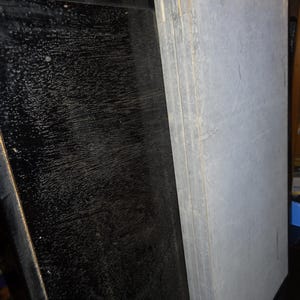 May include: A stack of gray panels with visible wood grain and a black panel with a textured surface. The panels are leaning against each other. The image also shows a glimpse of a traditional Japanese doll.