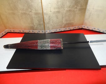 May include: A traditional Japanese folding umbrella with a red and white striped fabric canopy and a black wooden handle. The umbrella is closed and lying on a black surface.