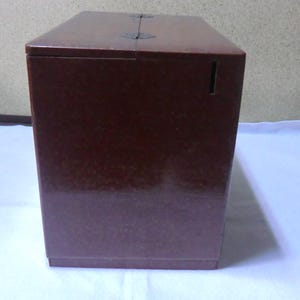May include: A dark brown wooden box with a hinged lid and a small slot on the front. The box has a textured surface and appears to be made of a high-quality material.