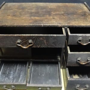 May include: A dark brown wooden chest with multiple drawers and a sliding door. The piece features a flat top surface, a large wide drawer at the top left, three smaller stacked drawers on the right, and two lower drawers at the bottom.