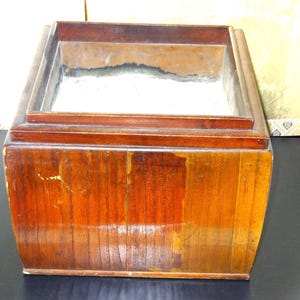 Könnte beinhalten: Eine Holzkiste mit einer rechteckigen Öffnung. Die Kiste ist aus dunklem Holz mit einer Maserung. Die Öffnung ist mit einem hellfarbenen Material ausgekleidet.